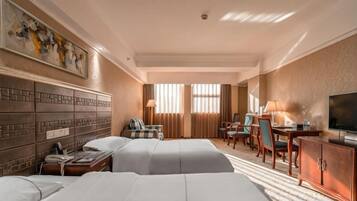 A hotel room with two beds, a desk, a chair, a TV, and a painting on the wall.