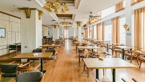 Un comedor amplio con mesas y sillas de madera, ventanas grandes con cortinas y un techo alto con candelabros.