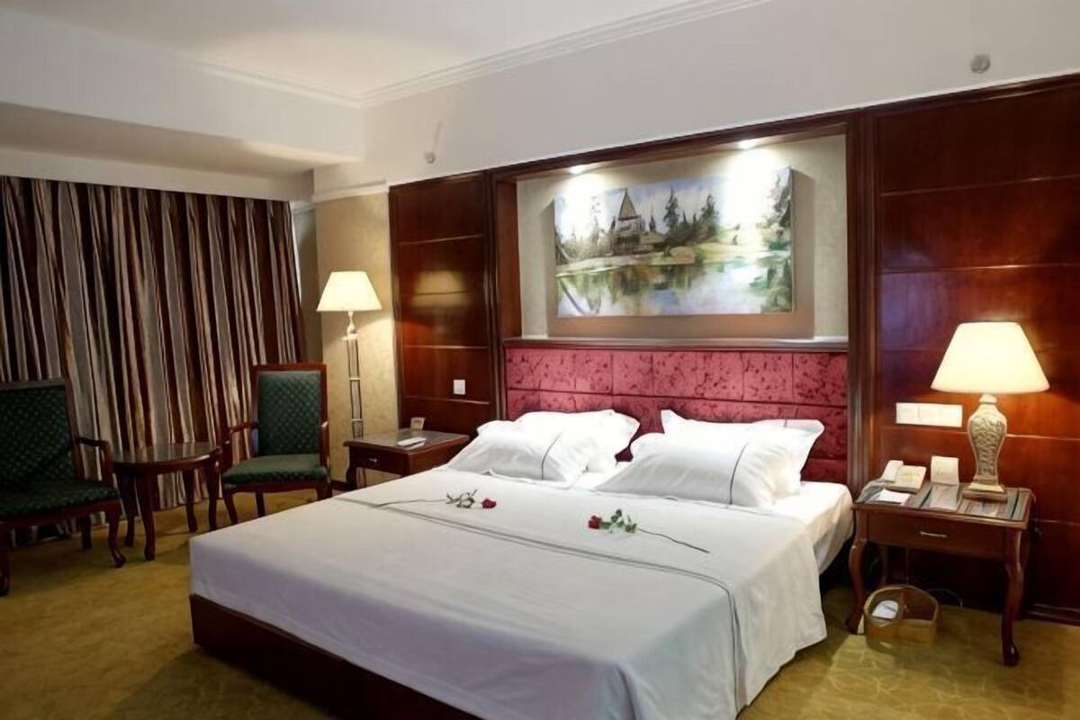 Quarto de hotel com uma cama grande, duas mesas de cabeceira, uma escrivaninha, uma cadeira e um quadro na parede.