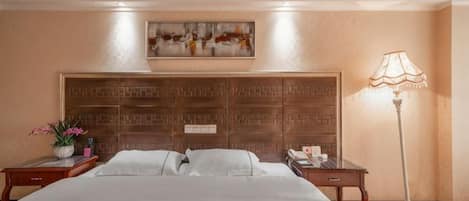 A hotel room with a large bed, a headboard with a geometric pattern, a bedside table with a lamp, and a painting on the wall.