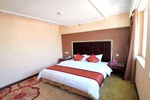 Habitación de hotel con una cama grande, una mesita de noche, un ventanal con cortinas y una alfombra estampada con motivos florales.