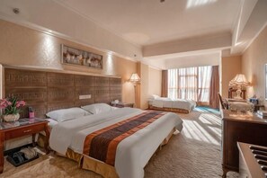 A hotel room with a large bed, a desk with a lamp, a chair, a piano, and a view of the outdoors. - Hengli Hotel (Panzhihua)