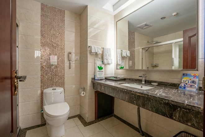 A bathroom with a toilet, sink, mirror, and tiled walls.