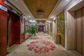 A hotel corridor with a patterned carpet, wooden walls, and a chandelier. - Hengli Hotel (Panzhihua)