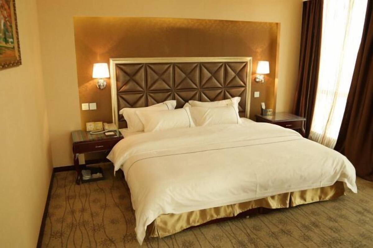 Quarto de hotel com uma cama grande, duas mesas de cabeceira, uma cabeceira e duas luminárias fixadas na parede.