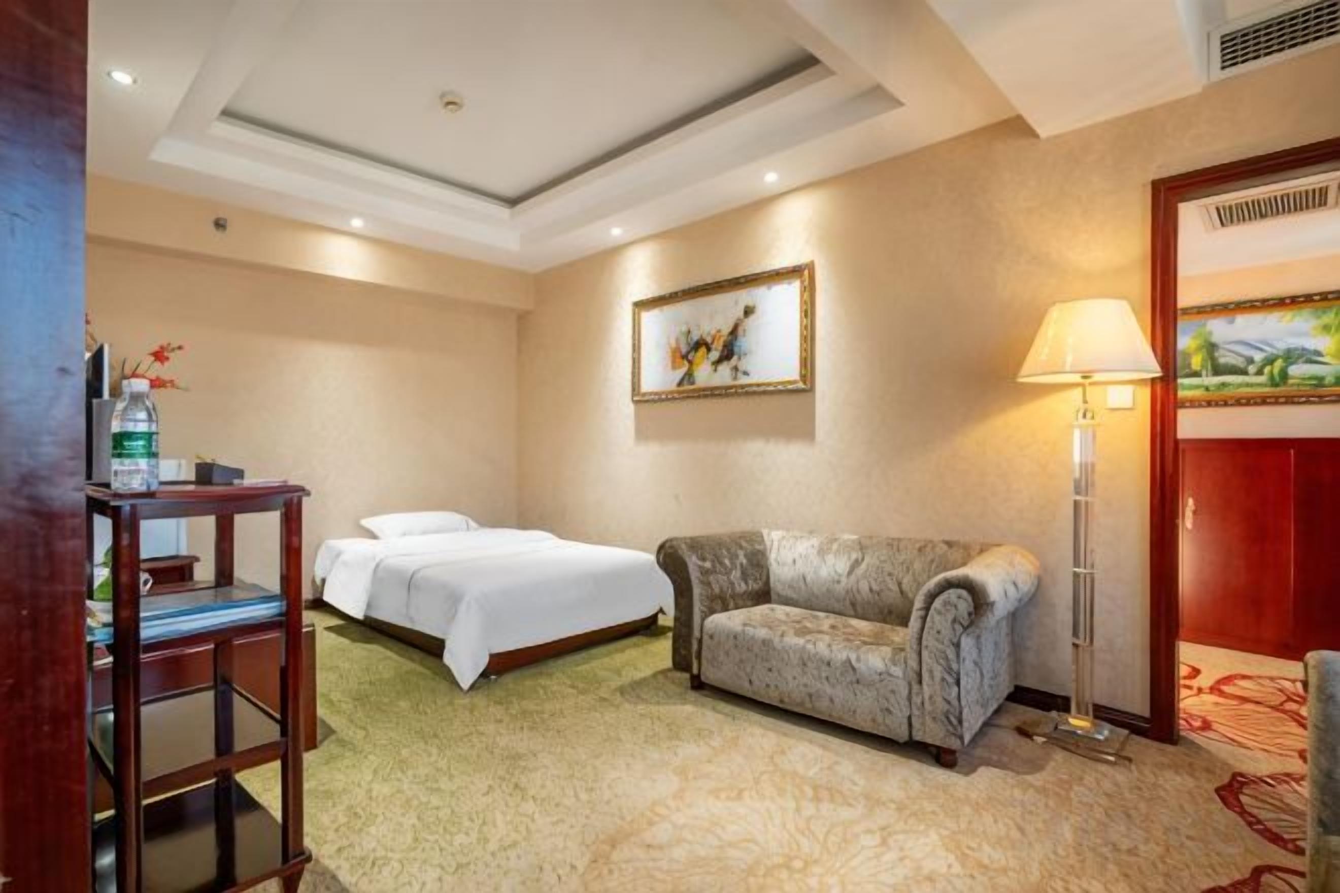 A hotel room with two beds, a sofa, a lamp, and a painting on the wall.