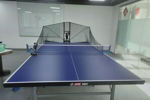 A ping pong table with a net in the center, a projector screen, and a glass wall with a red decoration. - Hengli Hotel (Panzhihua)