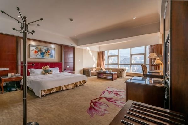 A hotel room with a large bed, a desk, a sofa, and a window with a view.
