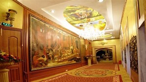 Un amplio pasillo con un gran mural, candelabros ornamentales y una alfombra estampada.