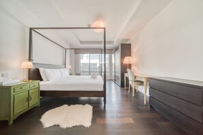 Une chambre moderne avec un lit à baldaquin, une table de chevet verte, un tapis blanc et moelleux, et une vue sur la ville grâce à de grandes fenêtres.