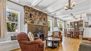A spacious living room with a brick fireplace, wooden flooring, and a dining area with wooden furniture.