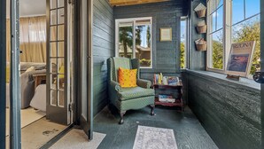 A cozy room with a green armchair, a small bookshelf, and a window with a view of trees.