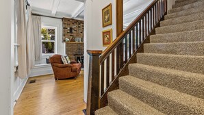 A staircase with a wooden handrail and carpeted steps leading to an upper floor. A brown leather armchair is positioned near a window with a view of the outdoors.