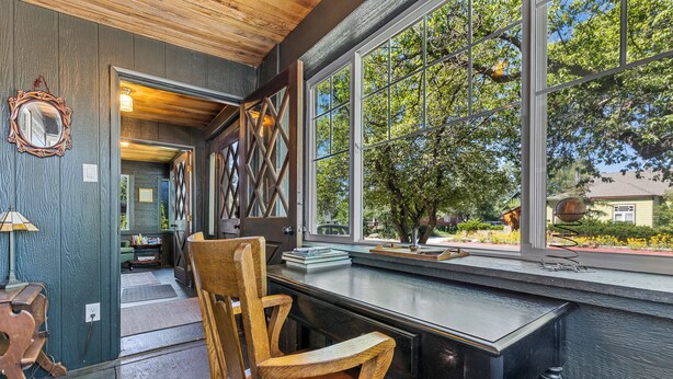 A wooden chair and a table in a room with a large window, a mirror, and a door leading to another room.