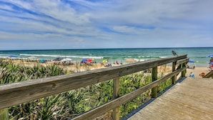 A wooden boardwalk leading to a beach with umbrellas and people.