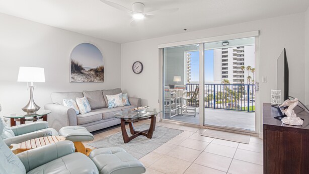 A modern living room with a sofa, armchairs, a coffee table, a TV, and a balcony with a view of a high-rise building.