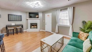 Un salon doté d’une cheminée, d’un canapé vert, d’une table basse blanche et d’un coin repas avec une table et des chaises.