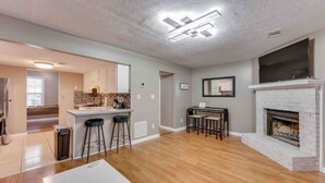 Un salon moderne avec une cheminée, un coin cuisine avec un mur de crédence en pierre et un coin repas avec une table et des chaises.