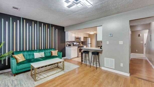 Un salon moderne avec un canapé vert, une table basse et une cuisine en arrière-plan.