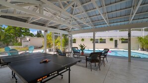 Ein überdachter Außenbereich mit Tischtennisplatte, Stühlen und Pool.