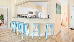 A modern kitchen with white cabinets, a central island with stools, and a view into the adjacent living area. - SaltyLux16 Heated Saltwater Pool/Near Beach/Island (Clearwater)