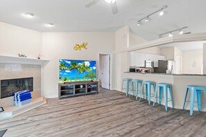 A modern living room with a fireplace, a TV, and a kitchen area with bar stools. - SaltyLux16 Heated Saltwater Pool/Near Beach/Island (Clearwater)