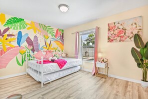 A bedroom with a bed, a bedside table, a window with curtains, a wall with a floral painting, and a large plant. - SaltyLux16 Heated Saltwater Pool/Near Beach/Island (Clearwater)