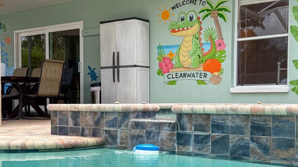 A pool area with a clear water feature, a welcome mural, and a stone-tiled edge. - SaltyLux16 Heated Saltwater Pool/Near Beach/Island (Clearwater)