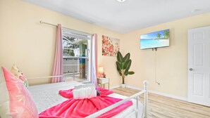 A bedroom with a bed, a window with curtains, a television on the wall, a door, and a plant. - SaltyLux16 Heated Saltwater Pool/Near Beach/Island (Clearwater)