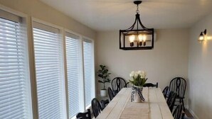 A dining room with a long table, black chairs, a chandelier, and large windows with blinds. - The White House Hub (Inkom)