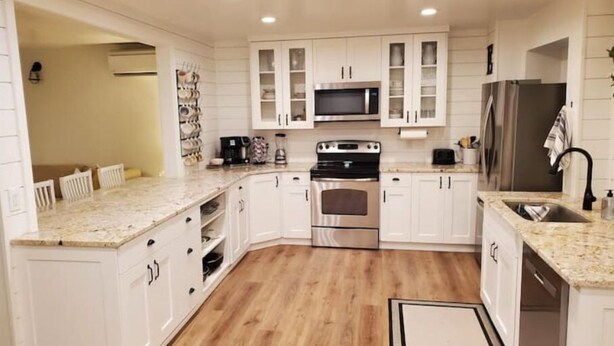 A modern kitchen with white cabinetry, stainless steel appliances, and a wooden floor. - The White House Hub (Inkom)