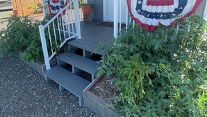 Ein Haus mit einer Veranda, Stufen zum Eingang und einem Gartenbereich mit Pflanzen.