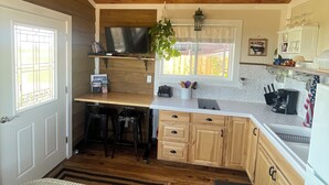Eine Küche mit Holzausstattung, Deckenventilator, Essbereich mit Tisch und Stühlen sowie eine kleine Sitzecke mit einem gewebten Hocker.