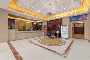 A hotel lobby with a reception desk, a chandelier, a vending machine, and a patterned carpet.