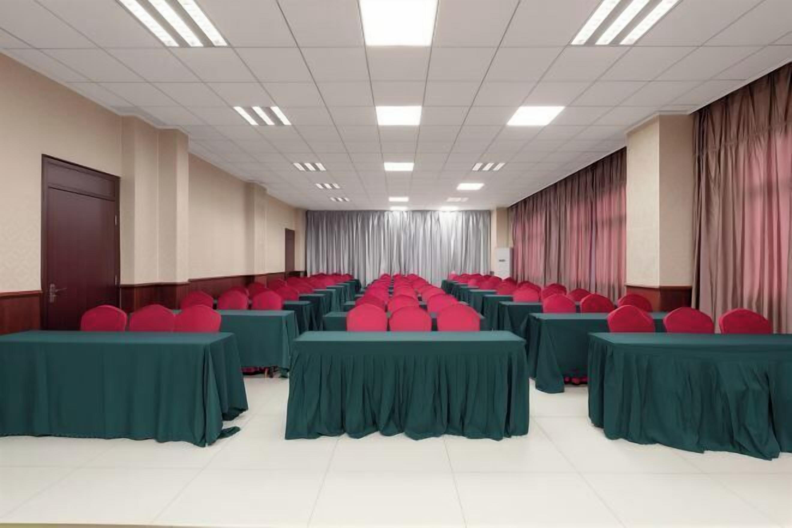 Un salón de conferencias con filas de mesas y sillas, una puerta a la izquierda y cortinas a la derecha.