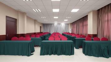Un salón de conferencias con filas de mesas y sillas, una puerta a la izquierda y cortinas a la derecha.