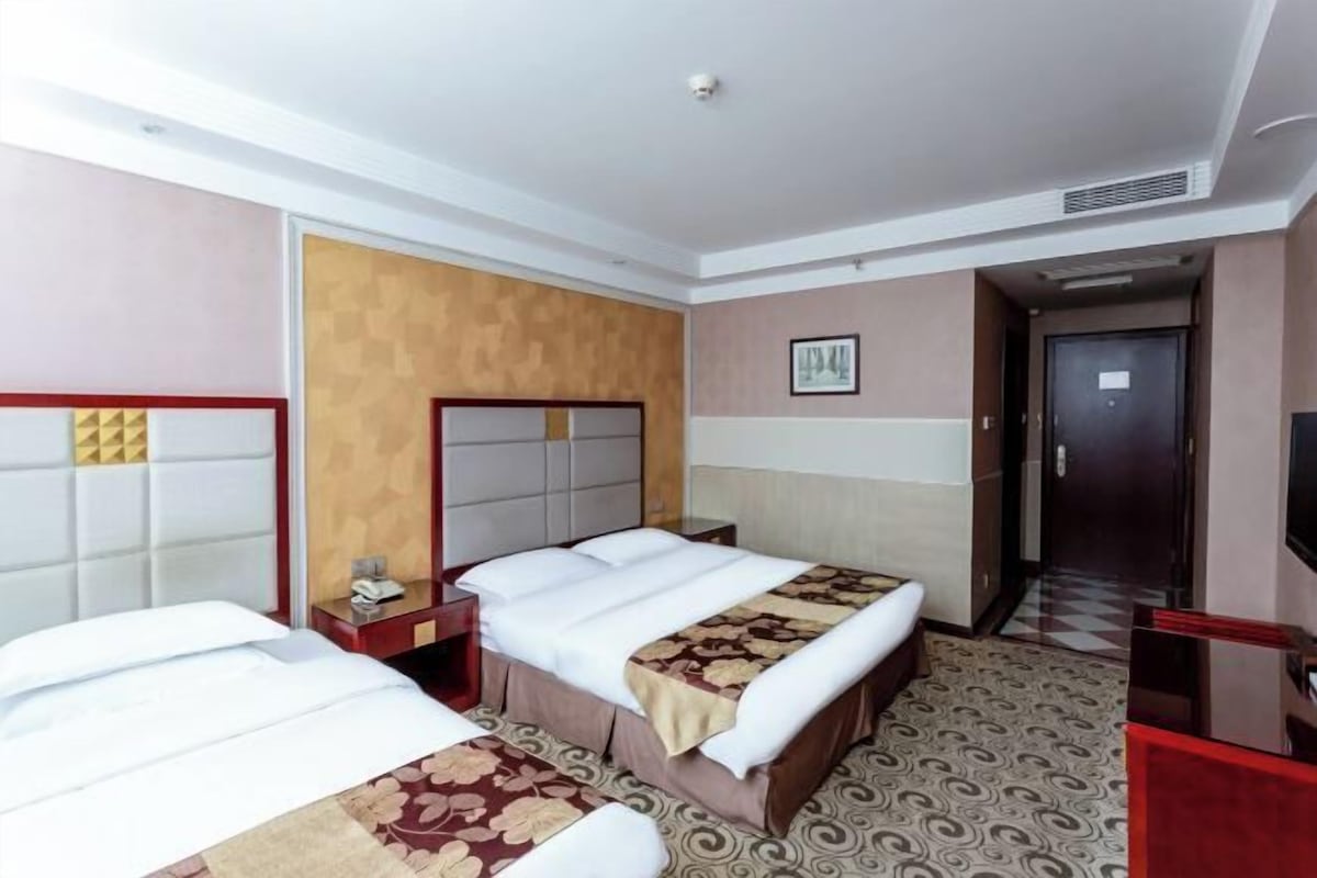 A hotel room with two beds, a wooden headboard, a small bedside table with a lamp, and a television on a stand.