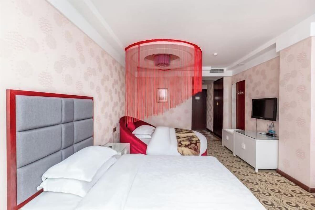 A hotel room with a large bed, a red canopy, a TV, and a desk.
