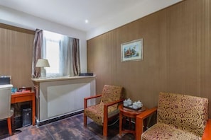 A hotel room with a desk, two patterned chairs, a small table with teapots, a window with curtains, and a framed picture on the wall. - Haotai Hotel (Ruian Jianye) (Lu'an)