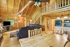 A wooden cabin interior with a living room, kitchen, and a staircase.