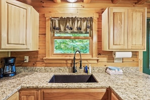 A kitchen with wooden cabinets, a granite countertop, a window with a view of greenery, a coffee maker, and a sink with a faucet.