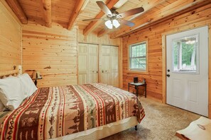 A wooden cabin bedroom with a bed, a ceiling fan, a window, and a door.