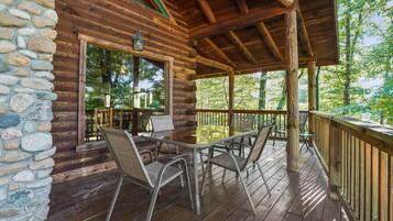 A wooden cabin with a stone wall, a covered porch, and a table with chairs.