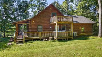 A two-story log cabin with a balcony, a porch, and a covered outdoor seating area.