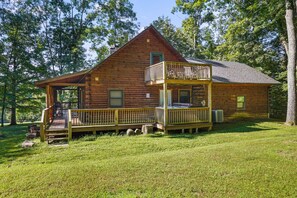 A wooden cabin with a balcony and a porch, surrounded by trees.