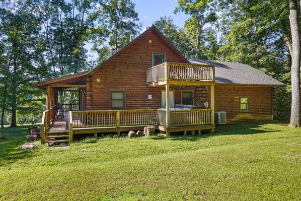 A two-story log cabin with a balcony, a porch, and a covered outdoor seating area.