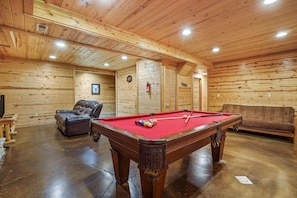 A wooden interior with a pool table, leather sofa, and a fireplace.