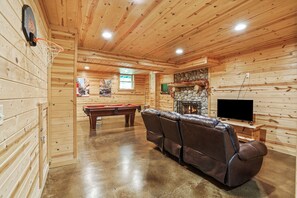 A wooden interior with a pool table, leather sofa, and a fireplace.