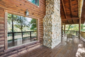 A wooden cabin with a stone pillar, large windows, and a deck with outdoor furniture.