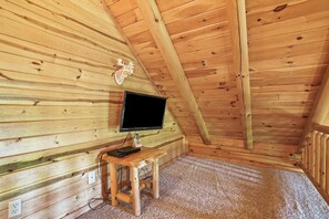 Une pièce de cabane en bois avec un plafond en pente, un téléviseur fixé au mur, une petite table en bois et une prise de courant.